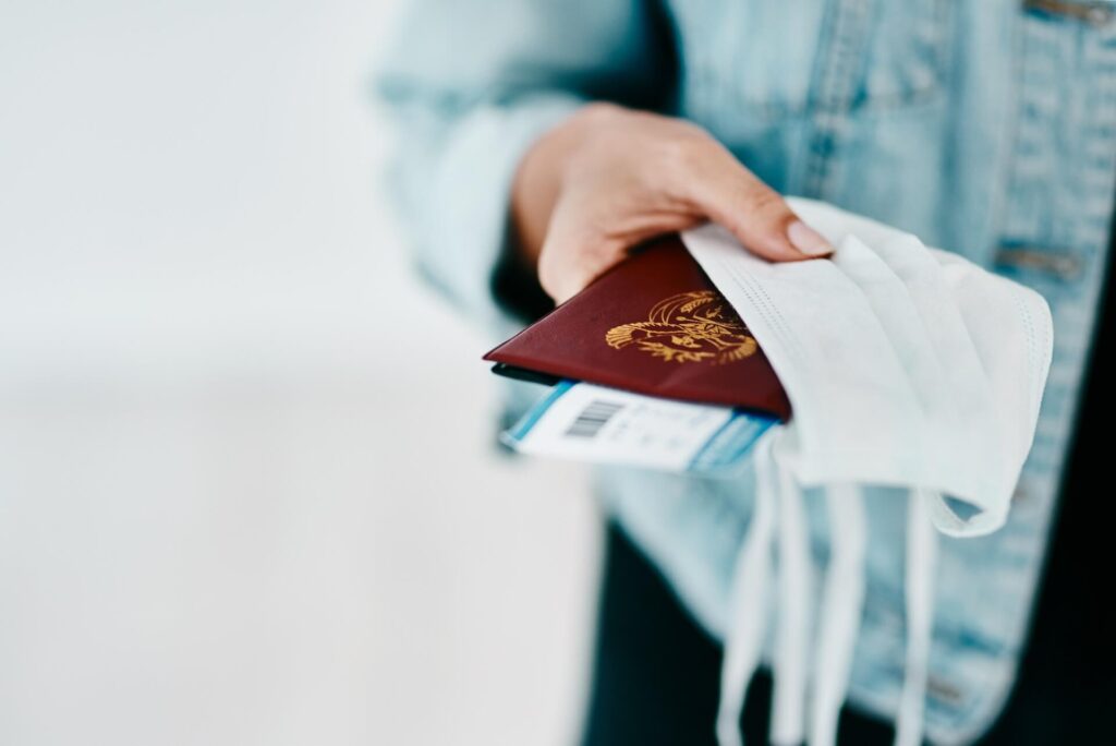 Cropped shot of a woman holding her passport, mask and boarding pass in an airport