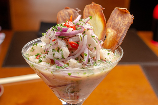 A close-up of a ceviche dish garnished with red onions, fresh cilantro, and red peppers, served in a vibrant presentation